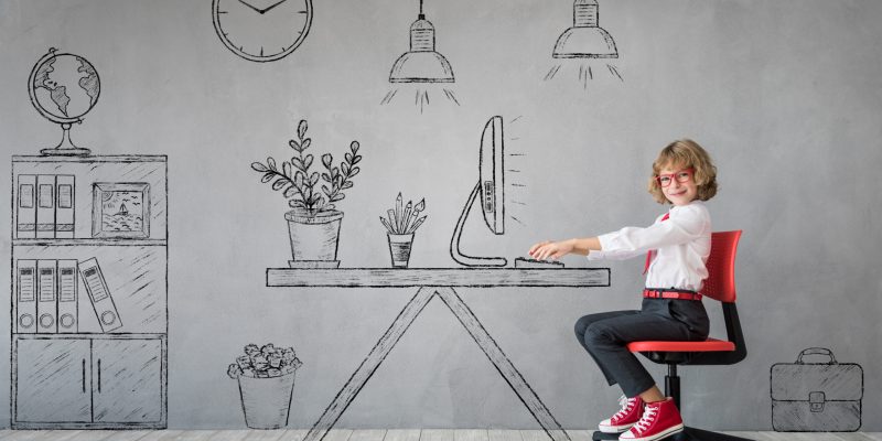 Happy child sitting at the desk in imaginary office. Business or education concept