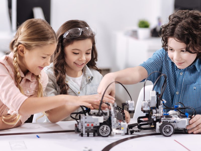 Delighted from project. Smiling upbeat optimistic children sitting at class and testing robot while working on the tech project